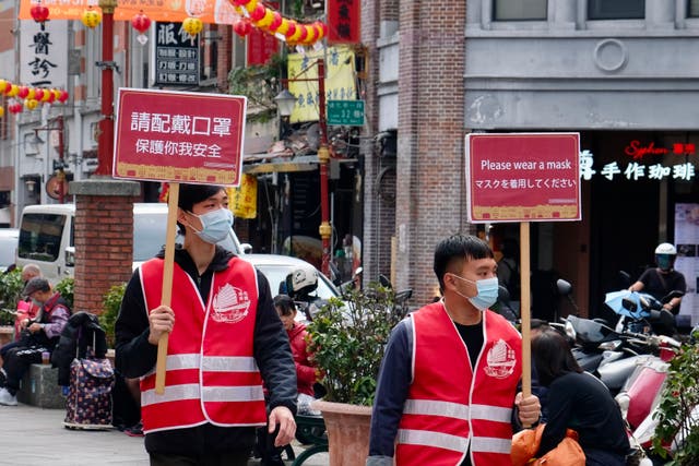 <p>Dos voluntarios caminan por el mercado tradicional de Dihua con carteles que piden que las personas usen máscaras en Taipei el 2 de febrero de 2021.</p>