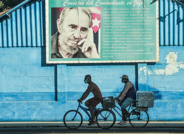 <p>Men ride on their bicycles near a poster of Cuban late leader Fidel Castro in Havana</p>