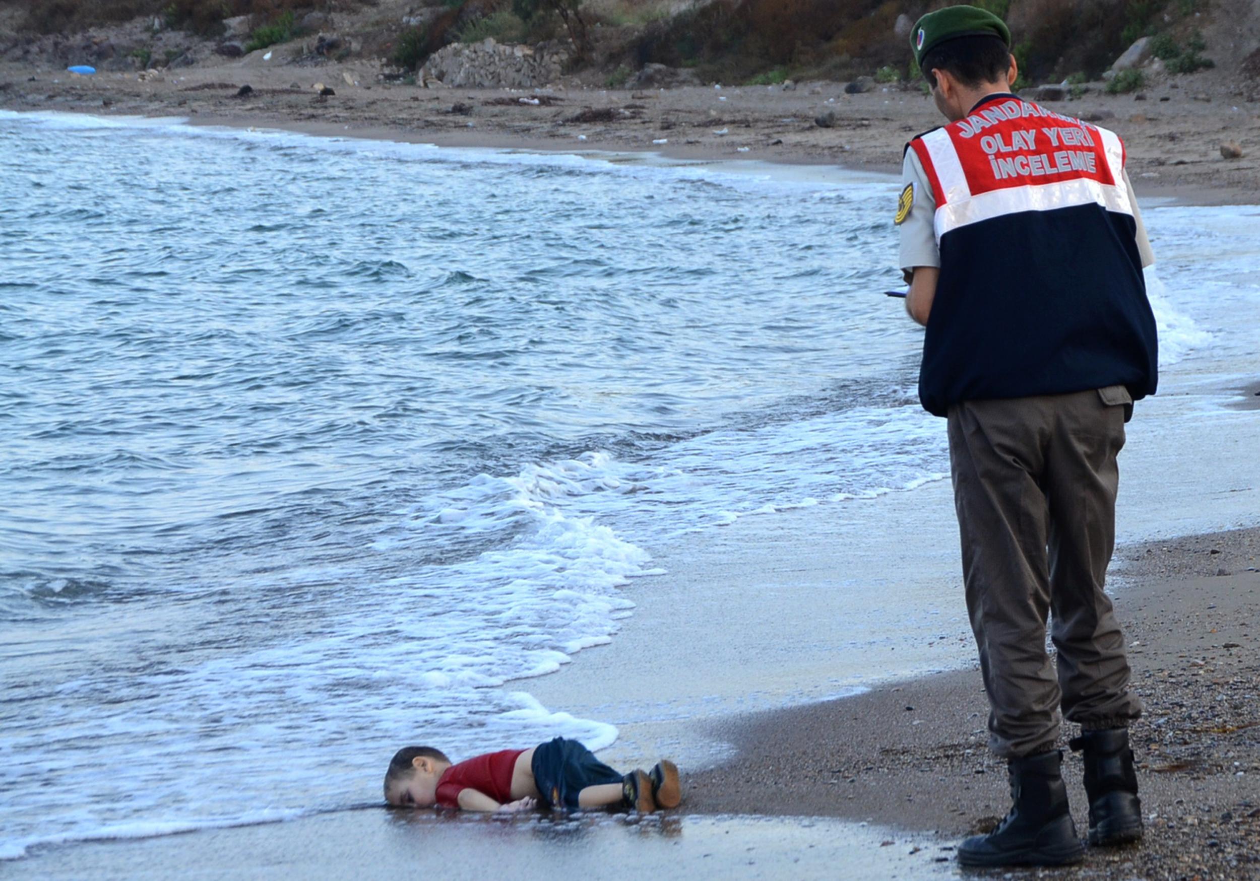 A Turkish police officer stands next to Alan Kurdi's body